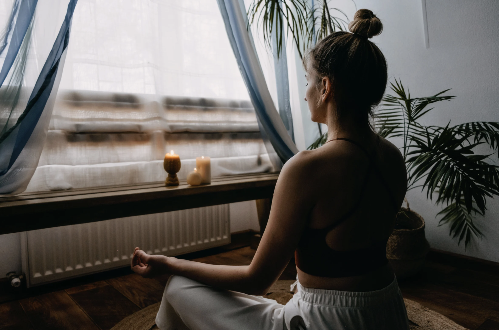 Woman meditating next to window with candles and incense.